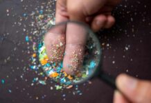 Terrifying Plastic Invasion: 90% of Cancer Tumors Hit A hand holding a magnifying glass over fingers covered in colorful particles