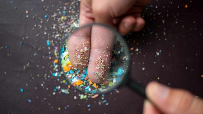 A hand holding a magnifying glass over fingers covered in colorful particles