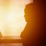 The Great Productivity Slump: What’s Really Happening? Silhouette of a person working on a laptop with sunlight streaming through blinds