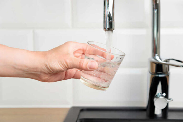 shutterstock2473504711jpg A hand holding a glass under a kitchen faucet as water is being poured into it
