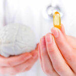 This Vitamin Deficiency Triggers Memory Decline A medical professional holding a brain model in one hand and a yellow supplement capsule in the other