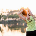 Exercise-Induced Bacteria: Are They Controlling You? A woman stretching her arms by a lake during sunrise