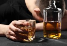 Alcohol’s Shocking Role in Breast Cancer A person with their head down, holding a glass of whiskey next to a bottle