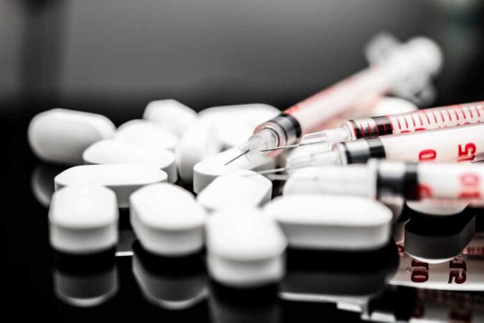 shutterstock_2478418051.jpg White pills and syringes arranged on a reflective surface