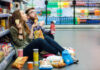 A young couple sitting on the floor of a grocery store enjoying snacks
