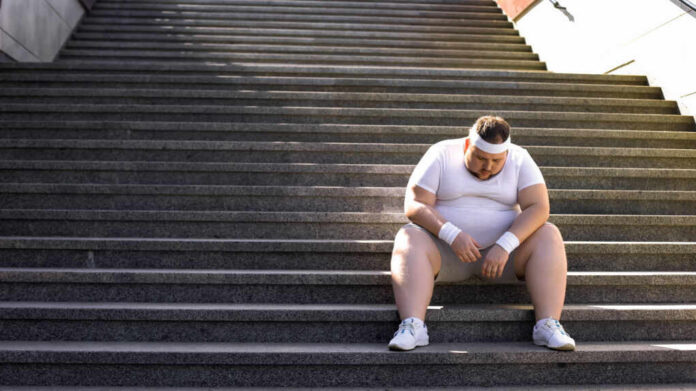 shutterstock_1271398939.jpg An exhausted man in sportswear sitting on outdoor stairs, looking down.