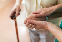 Simple Habits That Add Decades To Your Life Two hands clasped together, one elderly and one younger, with a cane in the background