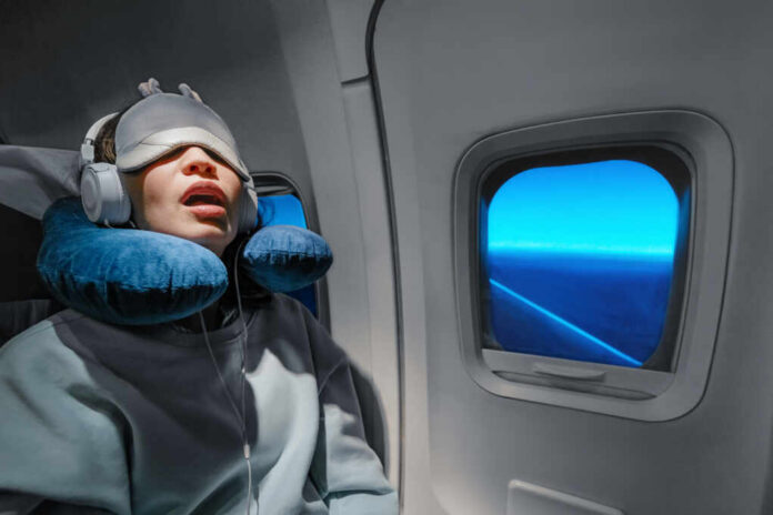 A passenger sleeping on an airplane with headphones and an eye mask