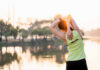 A woman stretching her arms by a lake during sunrise