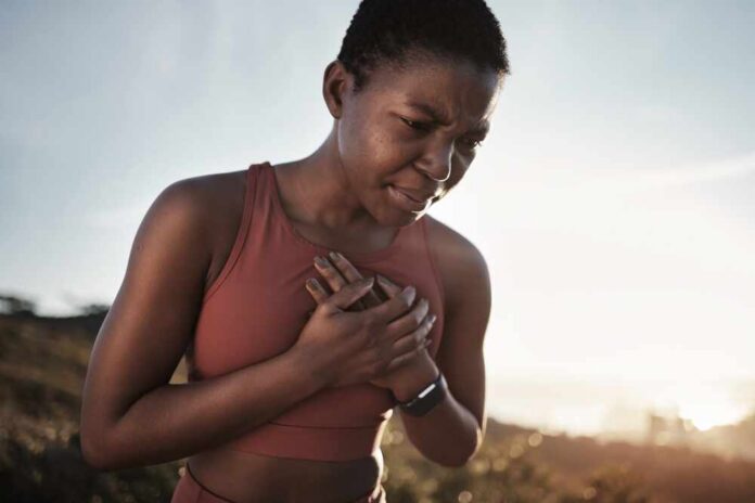 A woman in athletic wear holding her chest with a pained expression outdoors