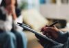 A therapist taking notes during a session with a client in the background