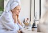 Dermatologists Expose Razor Lie Woman in a bathrobe with a towel on her head, smiling at her reflection in a mirror