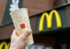 A hand holding a McDonalds beverage cup in front of the restaurants sign