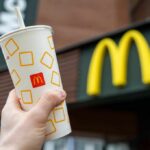 A hand holding a McDonalds beverage cup in front of the restaurants sign