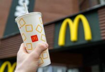 A hand holding a McDonalds beverage cup in front of the restaurants sign