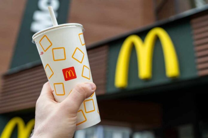 A hand holding a McDonalds beverage cup in front of the restaurants sign