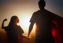 Child and adult in capes holding hands at sunset