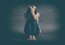 A person sitting on the floor with their arms wrapped around their knees, conveying a sense of distress