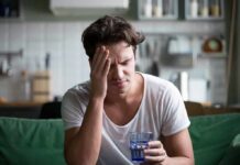 When Alcohol Turns Everyday Pills into a Dangerous Mix Man with headache holding a glass of water