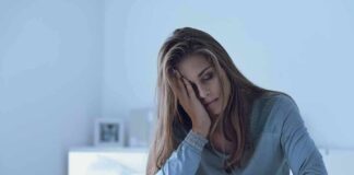 Woman sitting in bed with hand on face, looking tired