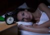 Woman lying awake in bed beside an alarm clock