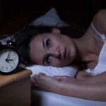 Woman lying awake in bed beside an alarm clock