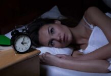 Woman lying awake in bed beside an alarm clock