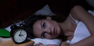 Woman lying awake in bed beside an alarm clock