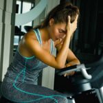 Exercise vs Antidepressants: What The Science Really Proves Woman resting on exercise bike with hand on forehead