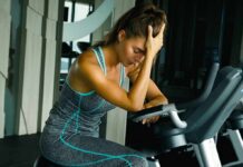 Woman resting on exercise bike with hand on forehead