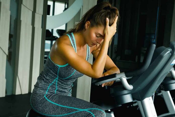 Woman resting on exercise bike with hand on forehead