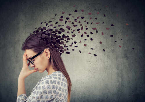 Memory,Loss,Due,To,Dementia,Or,Brain,Damage.,Young,Woman A woman with glasses holding her head, with fragments dispersing from her head