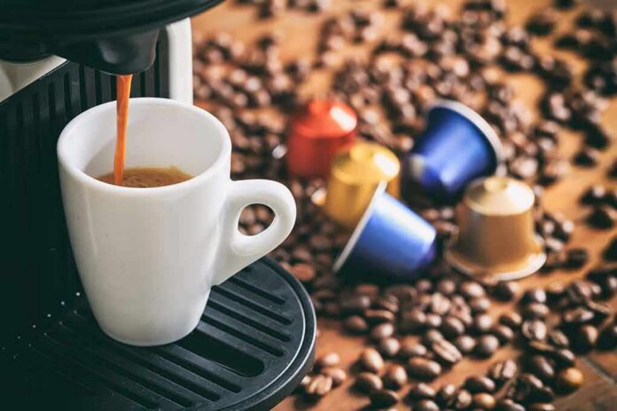 1783887703661-autbts-shutterstock-532833922 Espresso machine pouring coffee into a white cup with coffee pods and beans