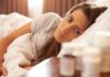 Woman lying in bed looking at pill bottles on a bedside table