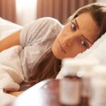 Woman lying in bed looking at pill bottles on a bedside table