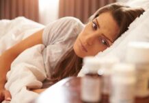Woman lying in bed looking at pill bottles on a bedside table