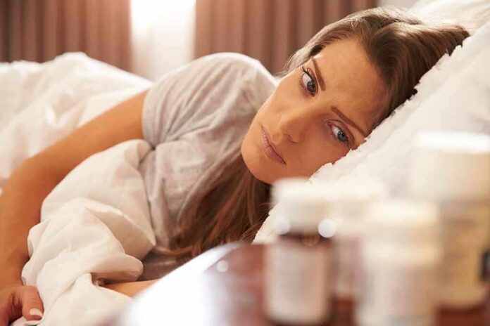 Woman lying in bed looking at pill bottles on a bedside table