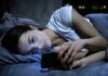 Woman lying in bed looking at a smartphone