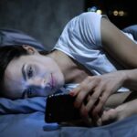 Woman lying in bed looking at a smartphone