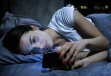 Woman lying in bed looking at a smartphone