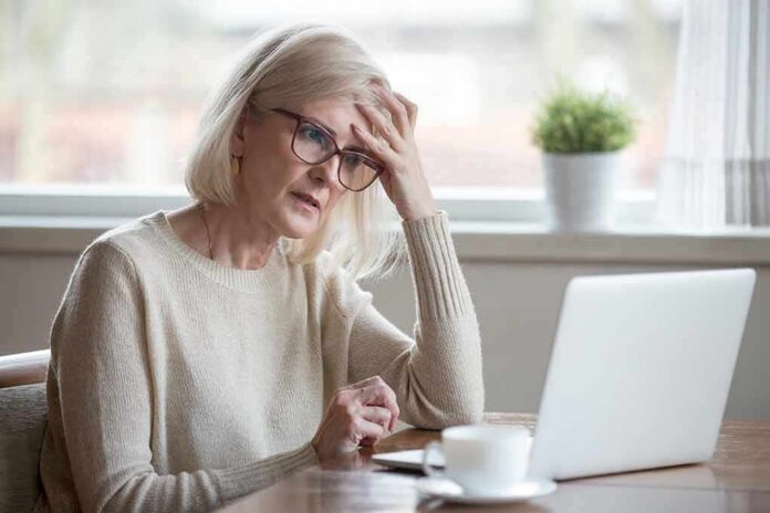 Older woman with glasses looking concerned at laptop