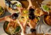 Hands clinking wine glasses over a dinner table