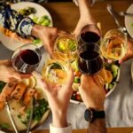 Hands clinking wine glasses over a dinner table