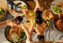 Hands clinking wine glasses over a dinner table