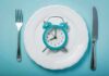 Best Weight Loss Strategy: Clock-Timed Eating vs Dieting Alarm clock on a white plate with fork and knife