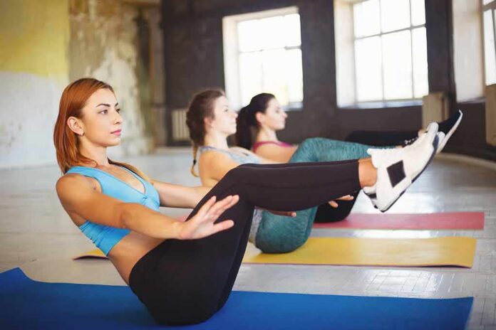 shutterstock_1149554819 Women practicing boat pose on yoga mats in a studio