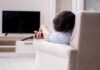 Person lying on a sofa holding a TV remote