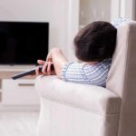 Too Much Sleep, Dementia Warning! Person lying on a sofa holding a TV remote