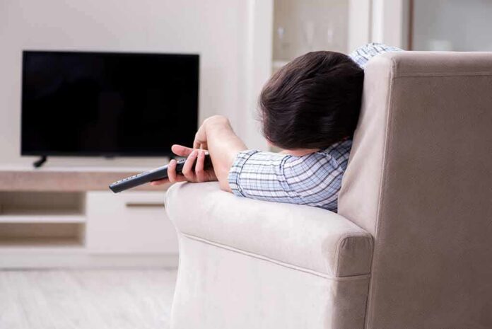 shutterstock_1166426527 Person lying on a sofa holding a TV remote