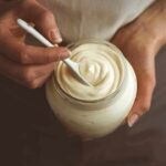Hands holding a jar of creamy yogurt with a spoon